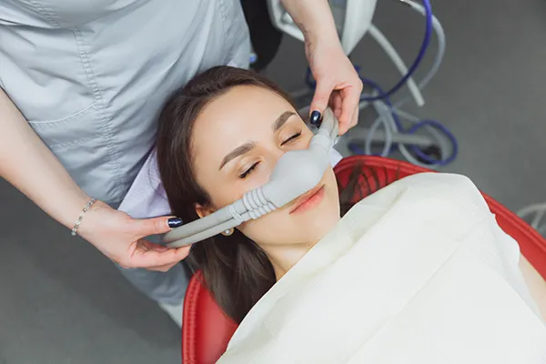 Dental assistant fitting a sedation mask over the nose of her calm female patient
